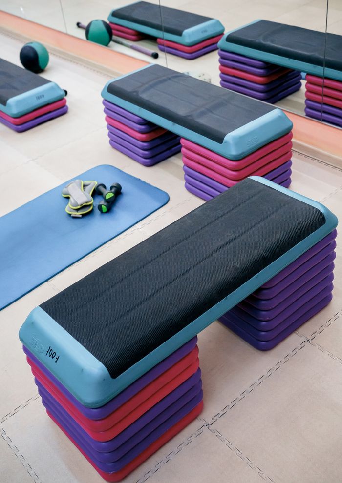 From above of modern fitness steps and mat with dumbbells placed on floor in front of mirror in sports club